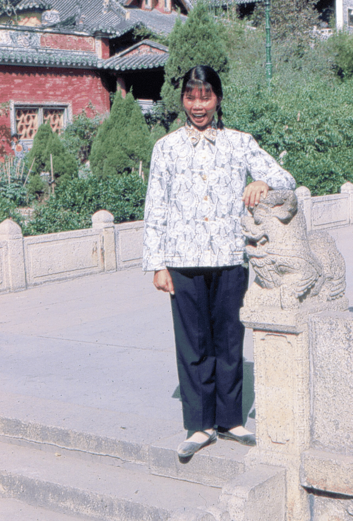 一位身着花衬衫的年轻女子站在石狮子旁微笑