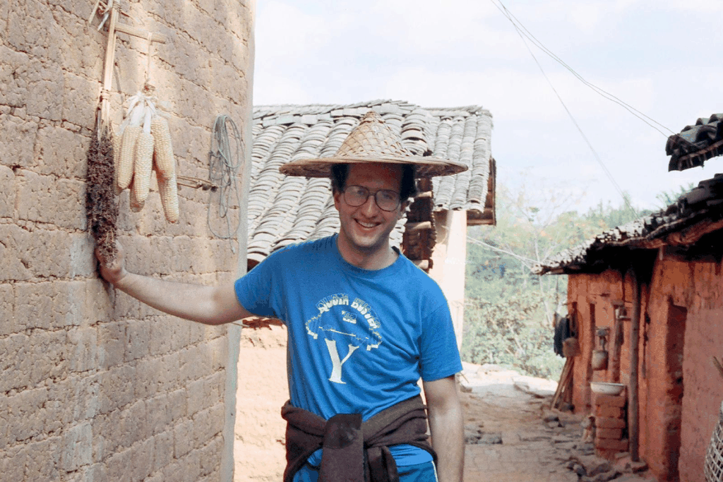 一位戴着斗笠的外国男子在土墙边微笑