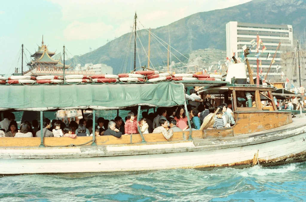 一张满载乘客的旧式街渡在碧波上行驶，背景是山峦与中式建筑