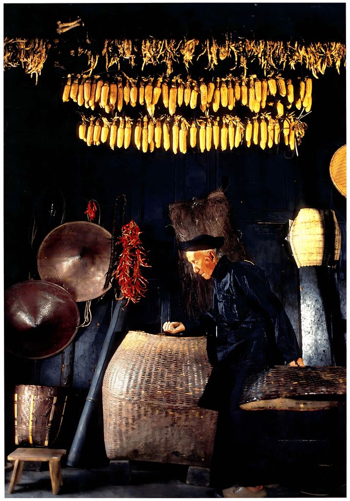 一位老人在挂满玉米和辣椒的屋檐下整理竹篓