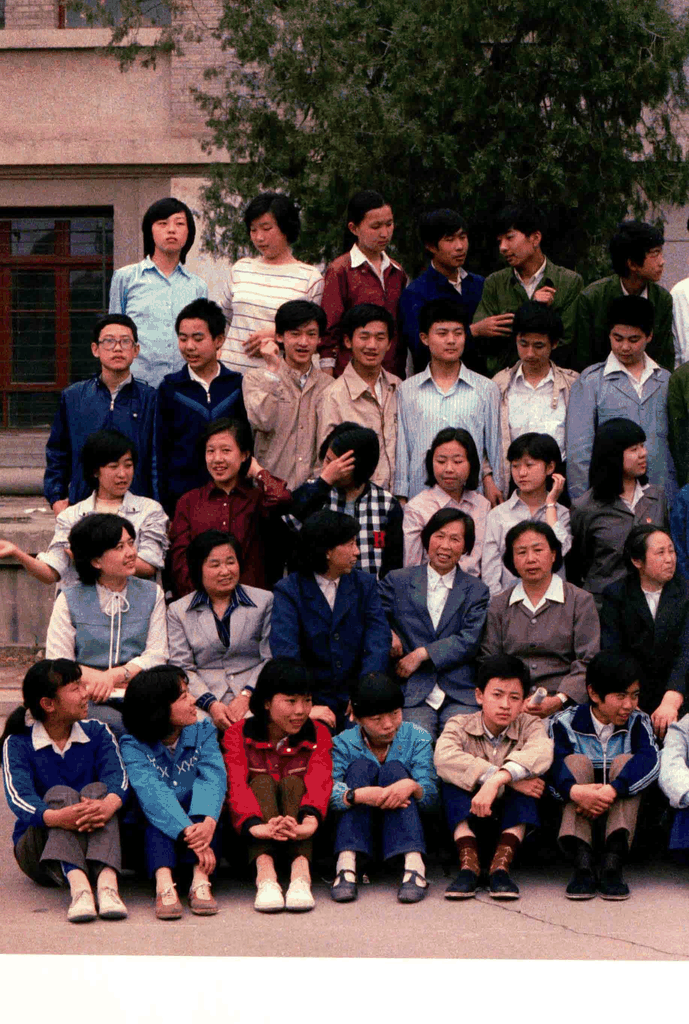 一张充满80年代气息的集体合影，背景是红砖建筑与绿树，人物穿着具有时代特征的服装