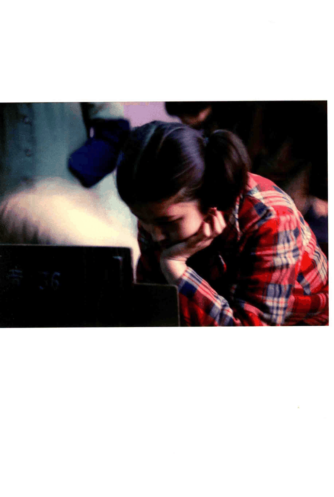 一位身着红蓝格纹衬衫的年轻女子在公共场所托腮小憩