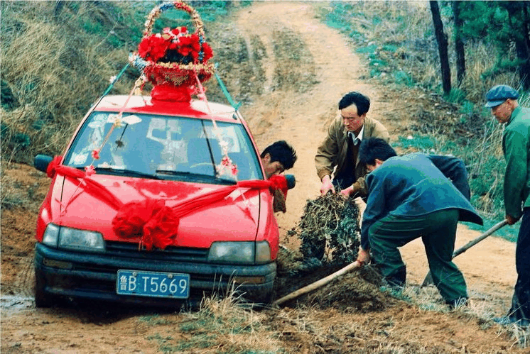一辆红色轿车陷入泥地,几位村民正在帮忙推车